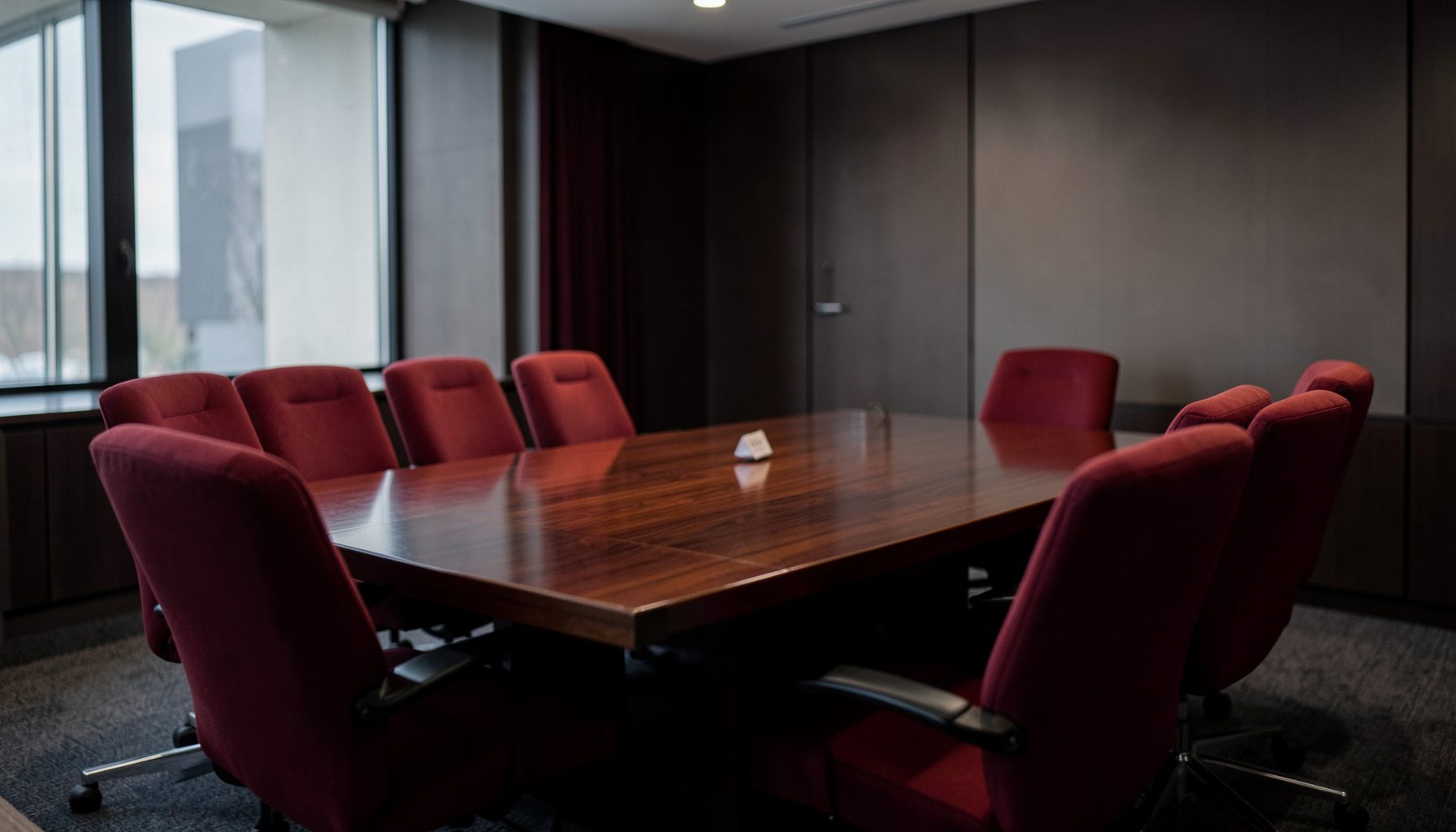 A softly lit conference room with a polished wood table and red upholstered chairs, conveying a serious and professional advocacy setting